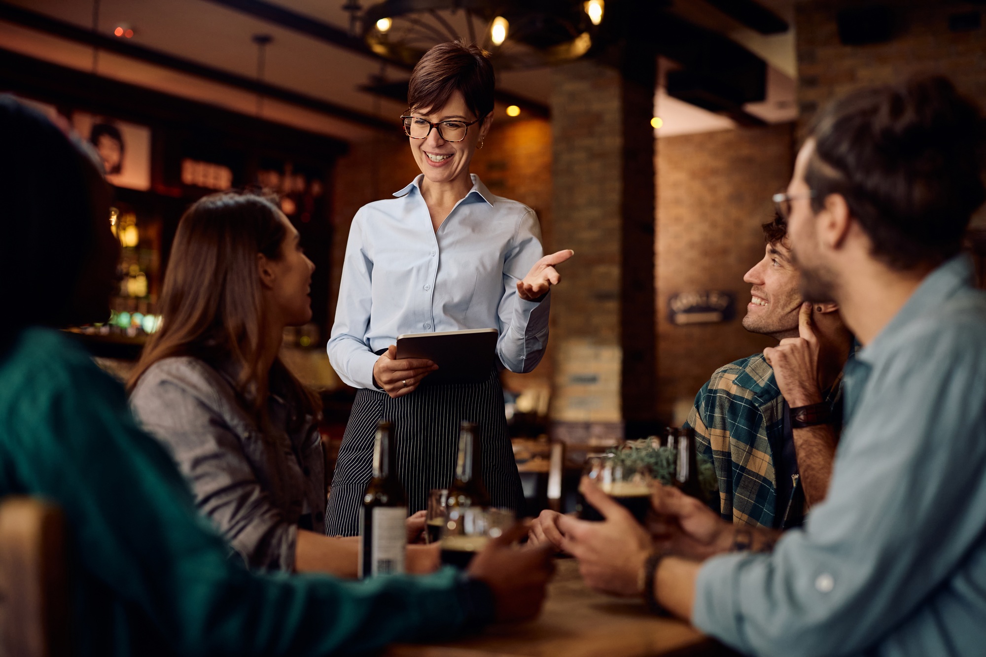 Happy waitress talking to group of guests in a bar.
